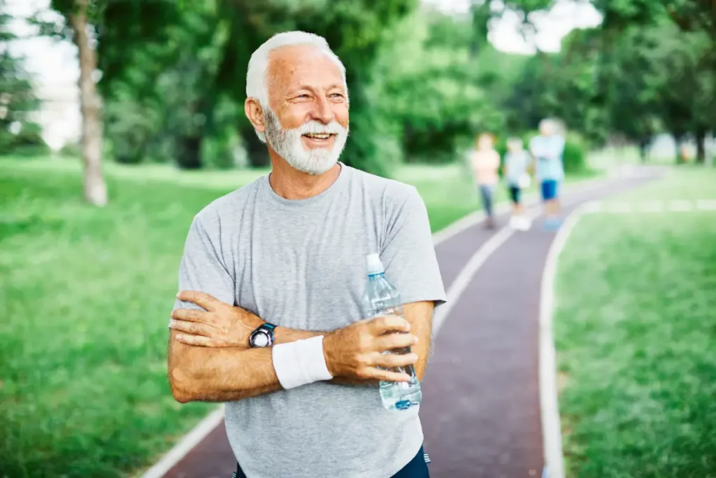 Mann beim Sport lächelt und hält eine Flasche Wasser in der Hand Prostatavergrößerung: Ursachen, Symptome & Tipps